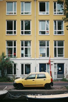A yellow car parked alongside a residential building by an Amsterdam canal.