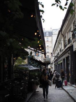 Cobblestone street with cafes and people walking in a narrow city alleyway.