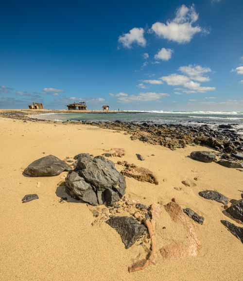 Free Beautiful sandy beach with rocky foreground, ocean view, and historic ruins on horizon. Stock Photo