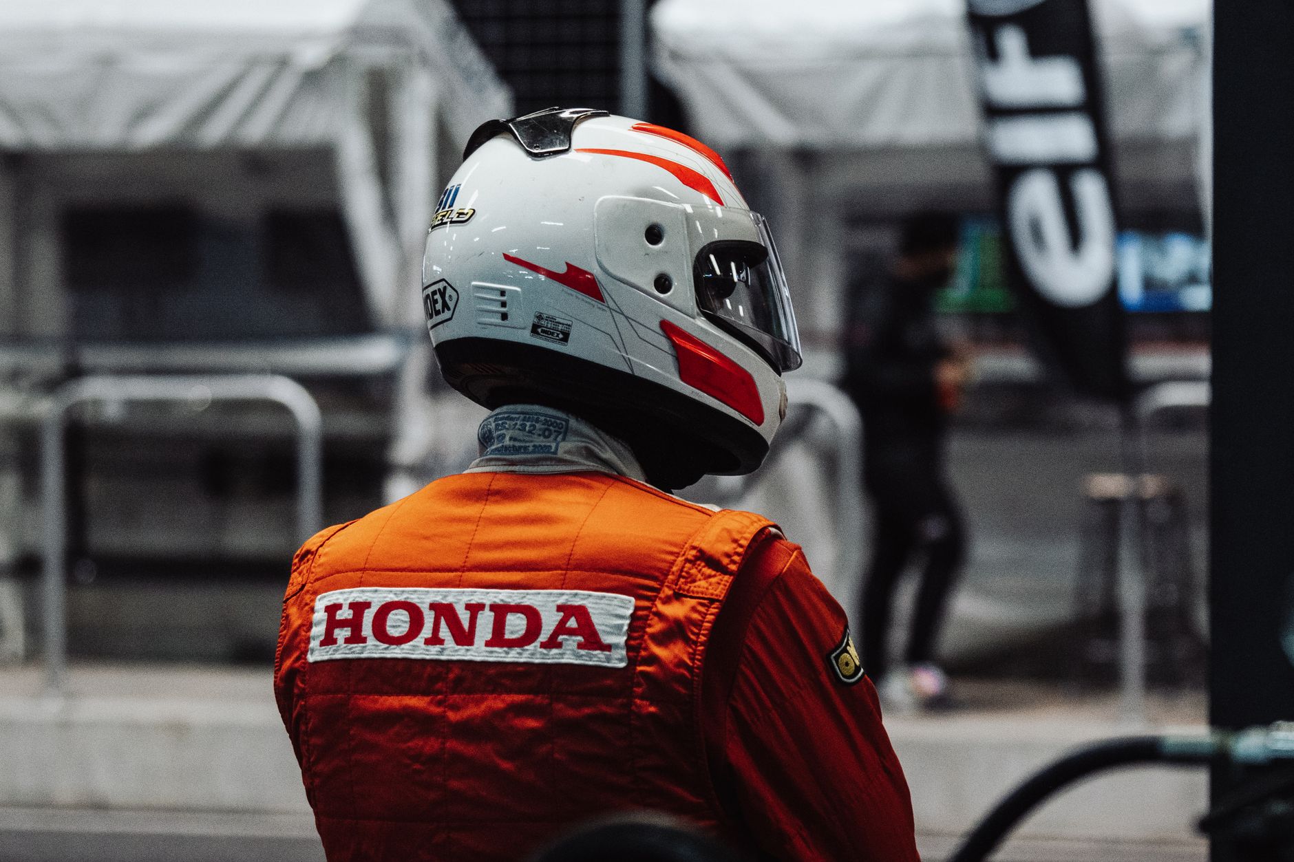A racecar driver in an orange jacket with a helmet, ready for a motorsport competition.