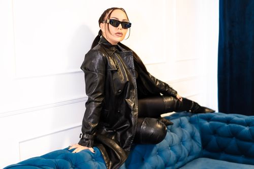 Free Fashionable woman in sunglasses poses stylishly on a blue sofa in a black leather outfit. Stock Photo