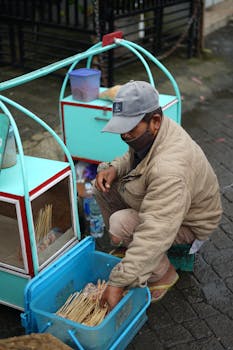 A street vendor in East Java arranges satay sticks by a turquoise cart, showcasing local food culture.