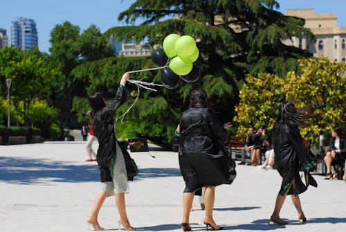 Three Women in Graduation Gowns Walking and Holding Balloons 