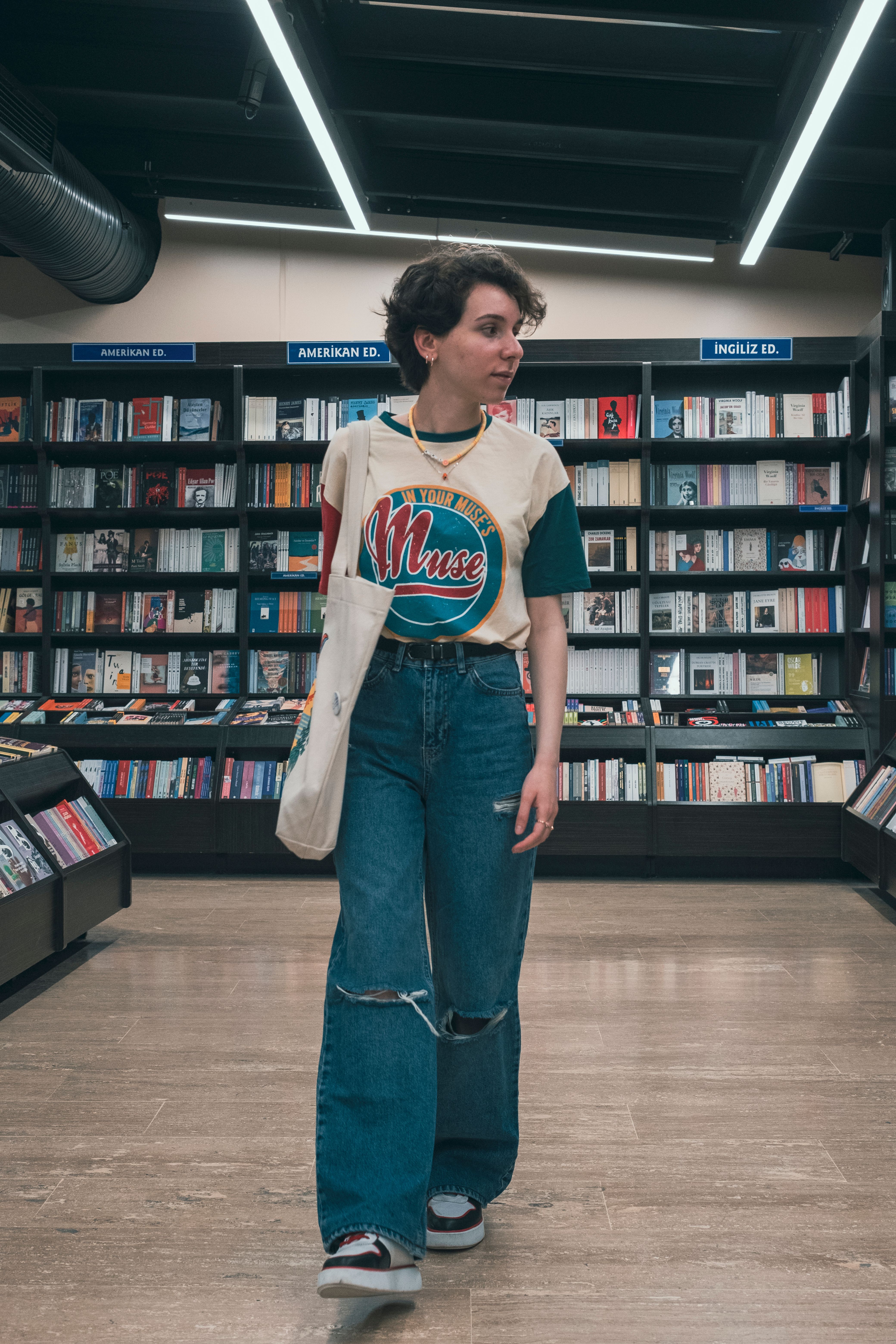 A stylish woman with a tote bag browsing books in a modern bookstore.
