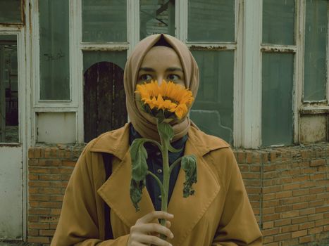 A woman in a hijab stands with a sunflower in front of her face in Ankara, Türkiye.