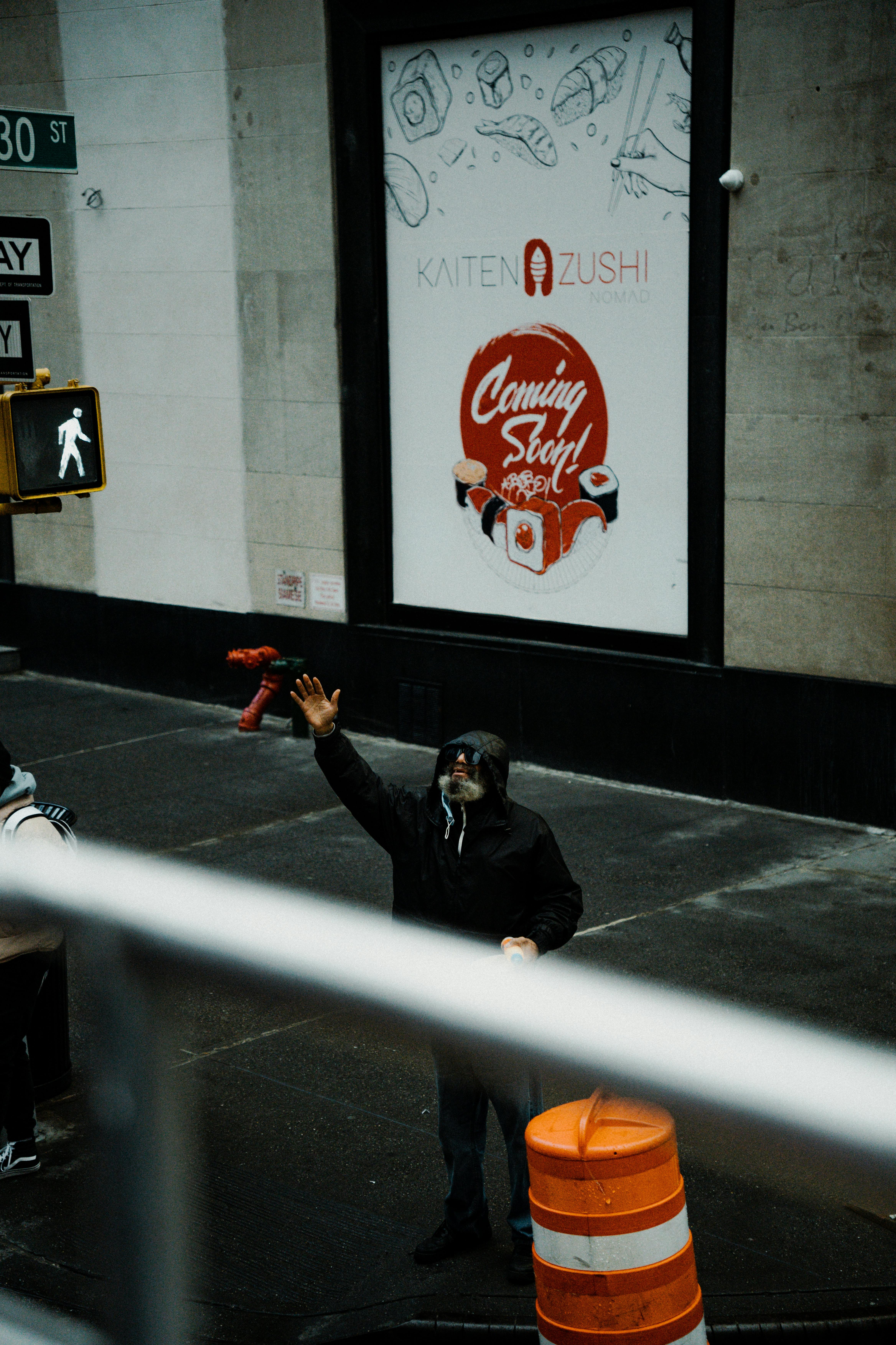 A person on a city street raises an arm near a 'Coming Soon' restaurant sign.