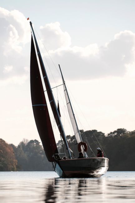 Sailboat navigating the Erdre River in autumn, near Sucé-sur-Erdre, France.