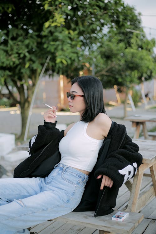 A Woman in Crop Top and Denim Pants Smoking a Cigarette