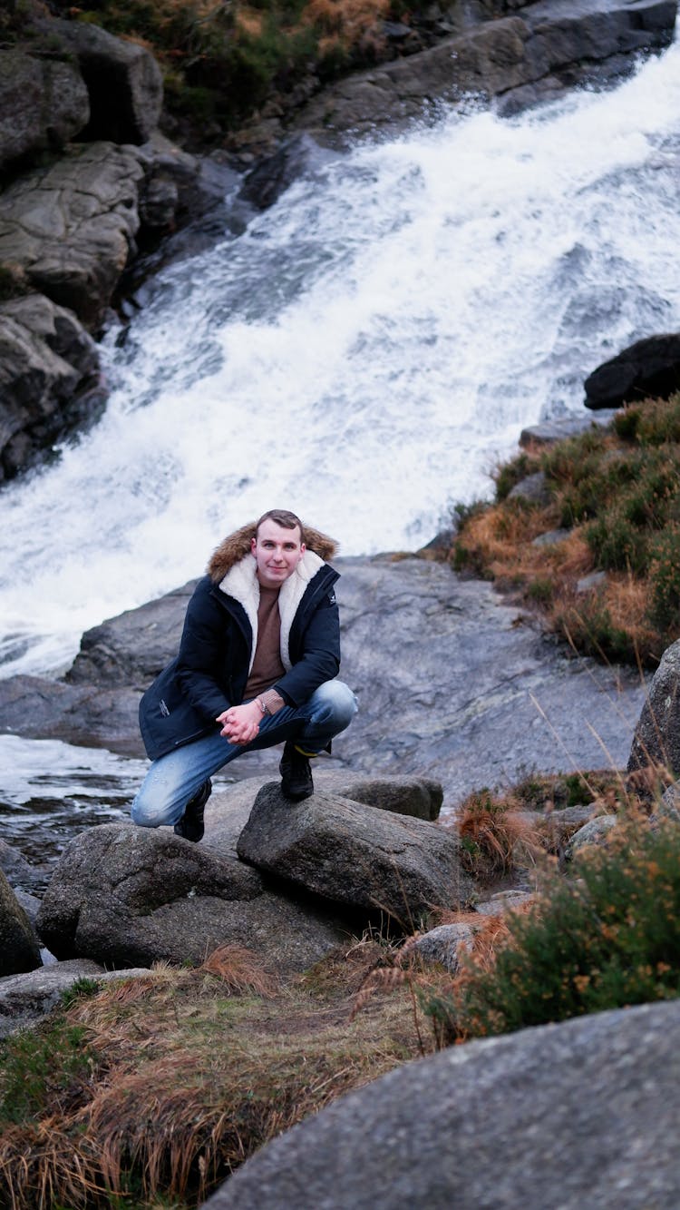 Man Squatting On Rock Near River