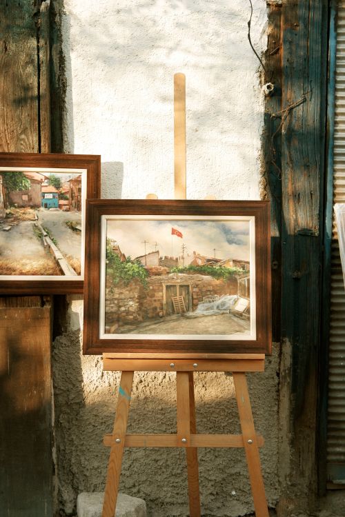 Free Two framed landscape paintings displayed on an easel against a rustic wall. Stock Photo