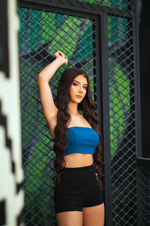 Free Confident woman in blue crop top leans against iron fence, showcasing fashion style. Stock Photo