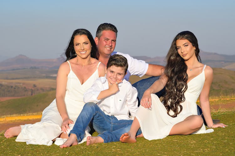 Family Dressed In White Posing For Photo Sitting On Grass