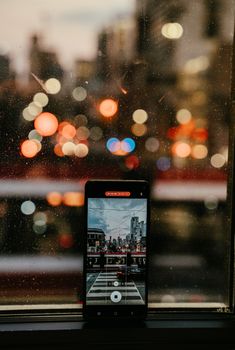 A smartphone captures a vibrant city street with bokeh lights at night in Toronto, ON, Canada.