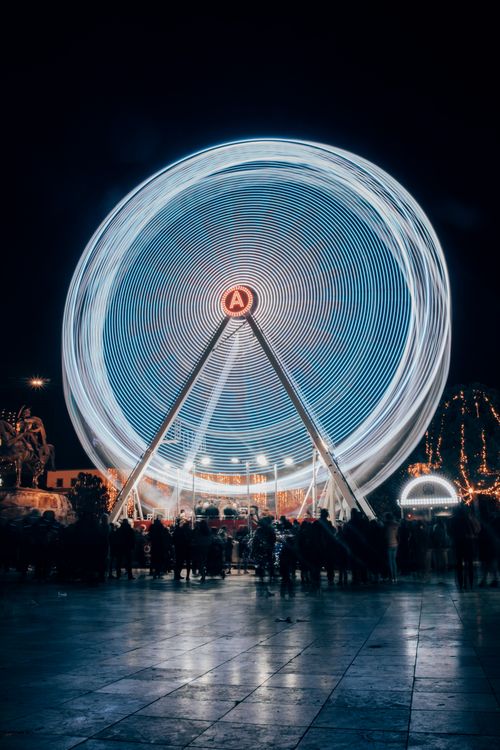 Free A captivating view of a brightly lit Ferris wheel in motion against the night sky, surrounded by a lively crowd. Stock Photo