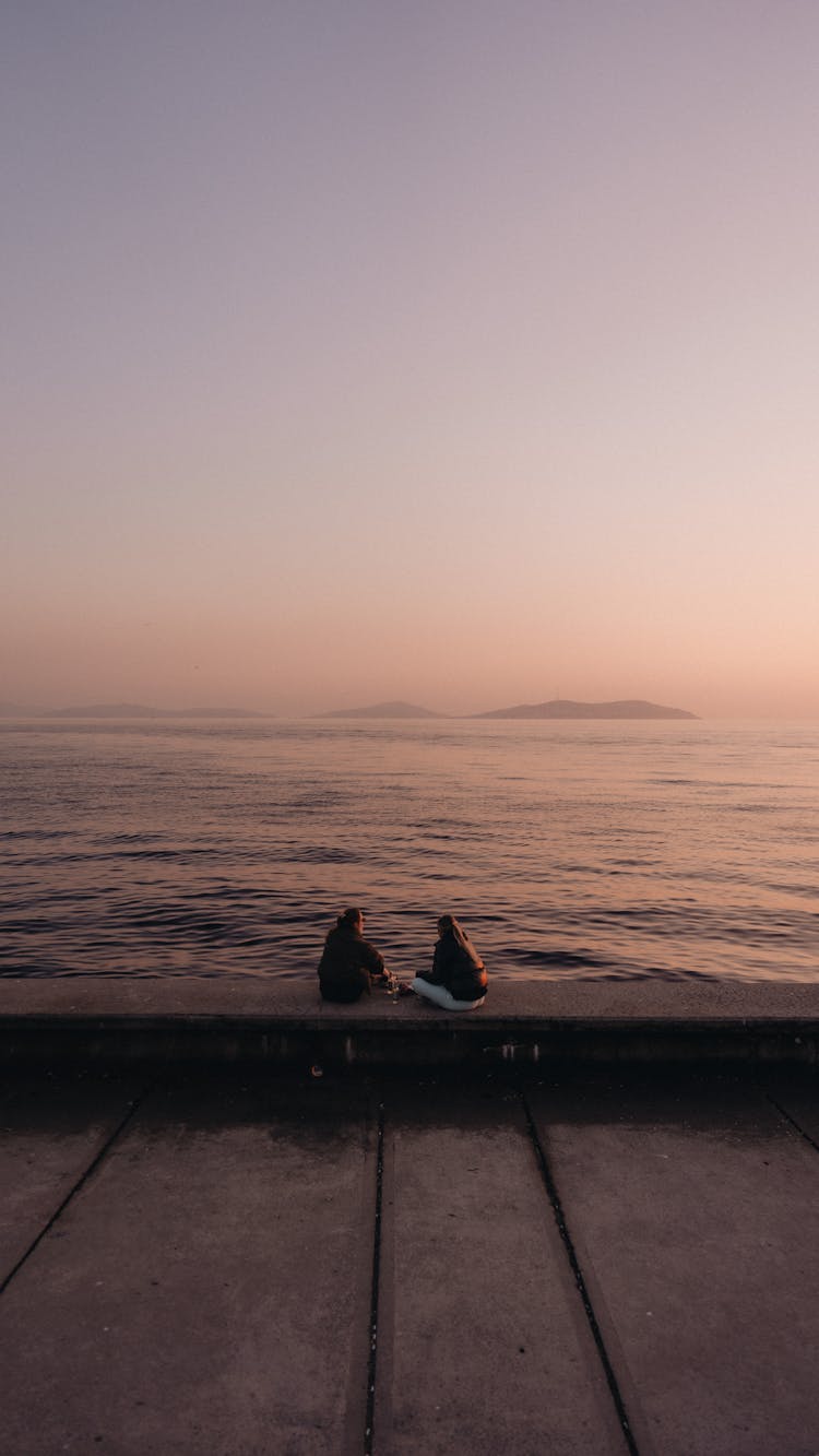 Women Sitting On A Pier At Sunset