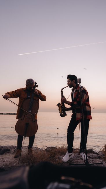 Two musicians play cello and saxophone by the Istanbul seaside during a sunset.