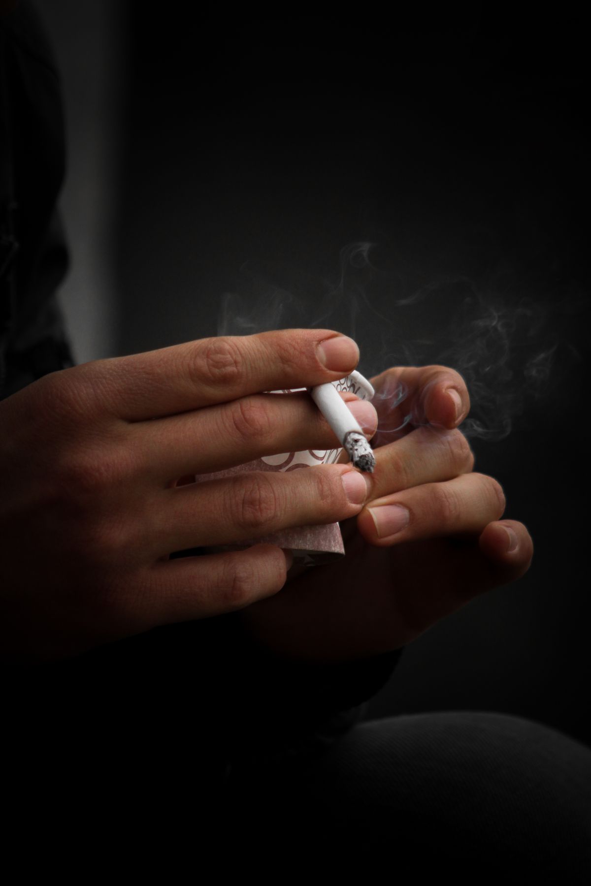 Mãos segurando cigarro aceso, mostrando o hábito de fumar de forma direta e educativa