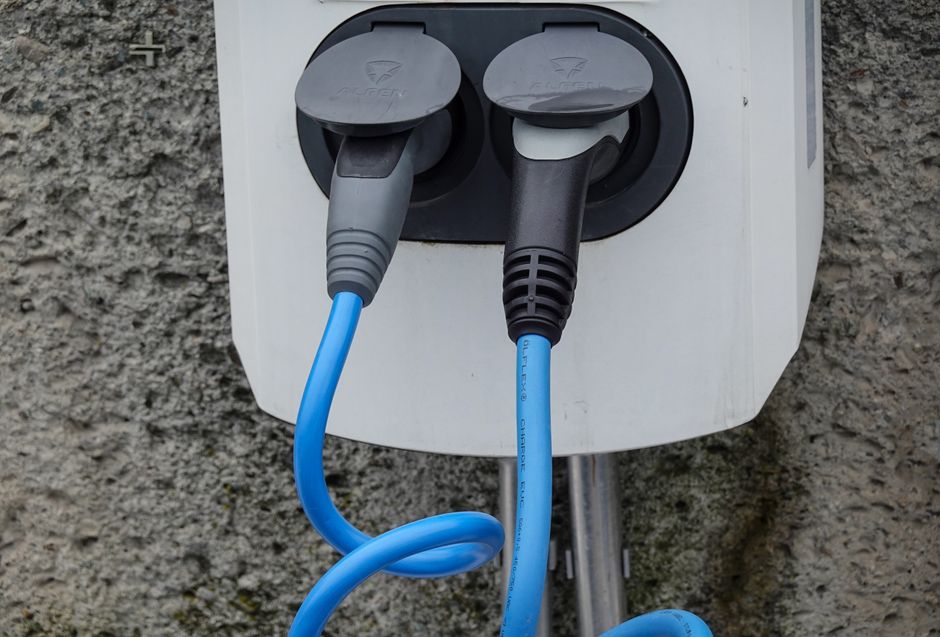 Bluetti - La marque montante des stations électriques Close-up of an electric vehicle charging station with two cables in sockets against a textured wall.