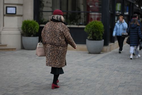 Free Woman in leopard coat with red accessories strolling urban sidewalk. Stock Photo