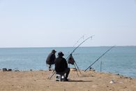 Two men fishing by the seaside on a clear day, enjoying leisure time.