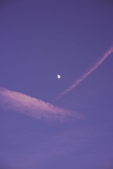 A tranquil evening sky featuring the moon and a contrail against a purple backdrop, perfect for wallpaper.