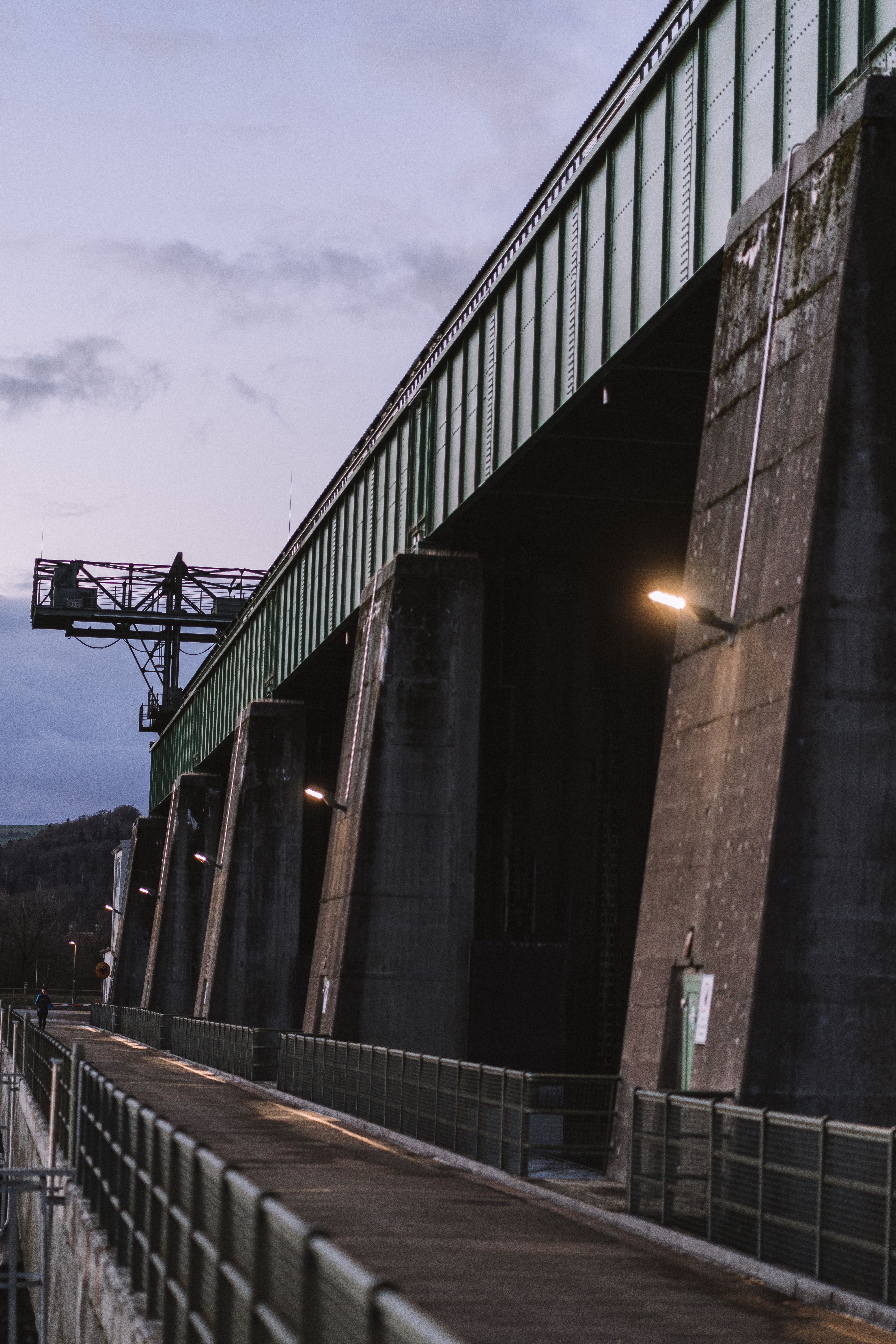 Dramatic view of a large industrial bridge at dusk with moody lighting and cloudy sky.