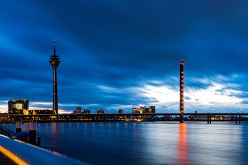 Free Captivating cityscape of Düsseldorf at night showcasing the illuminated Rheinturm and bridge reflections on the Rhine River. Stock Photo
