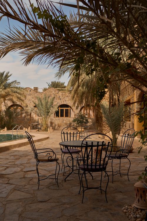 Free Serene Merzouga courtyard with iron patio set, palm trees, and rustic walls. Perfect for travel and architecture themes. Stock Photo