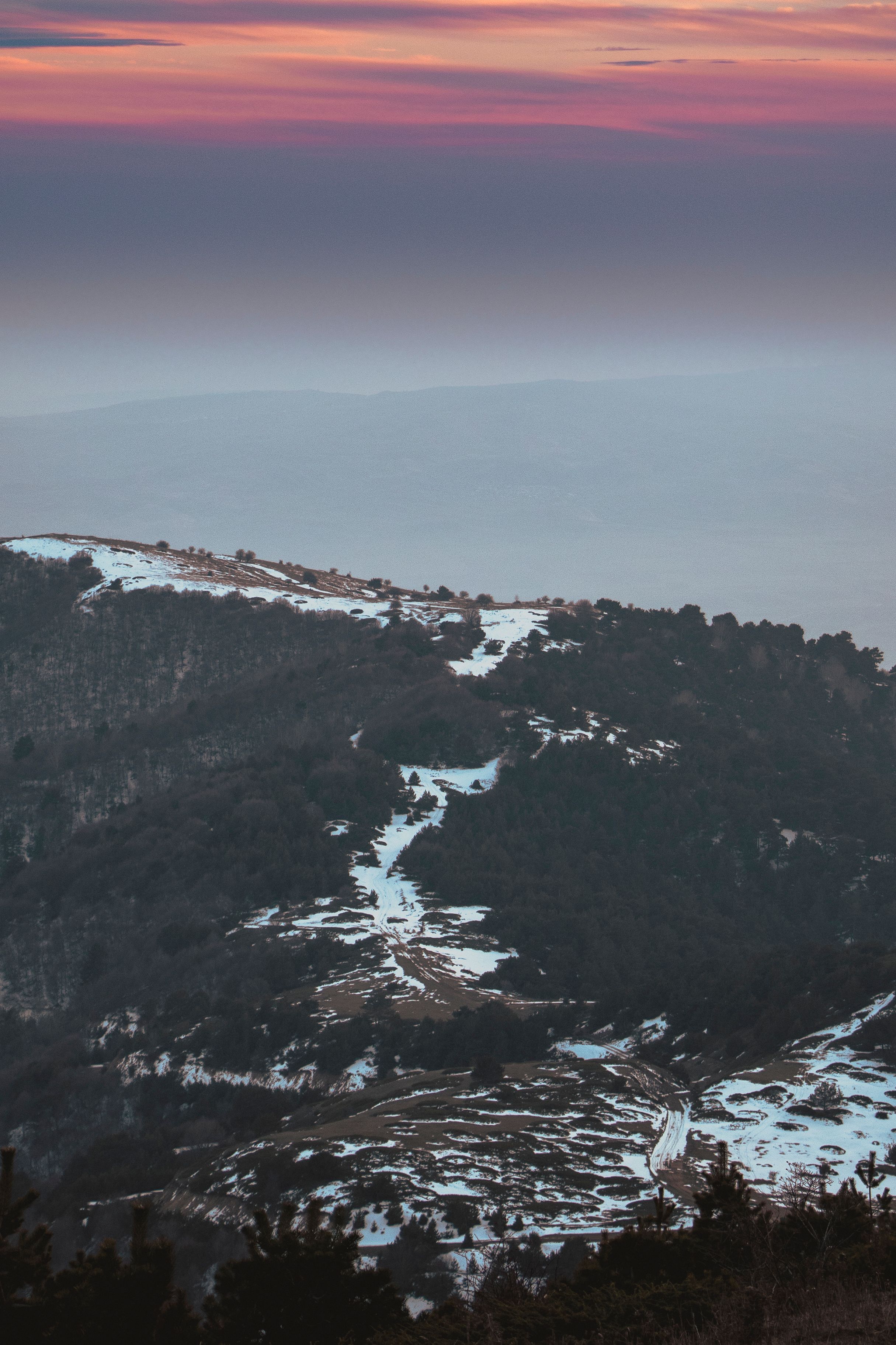 A breathtaking aerial view of snowy mountains and forests at sunset.