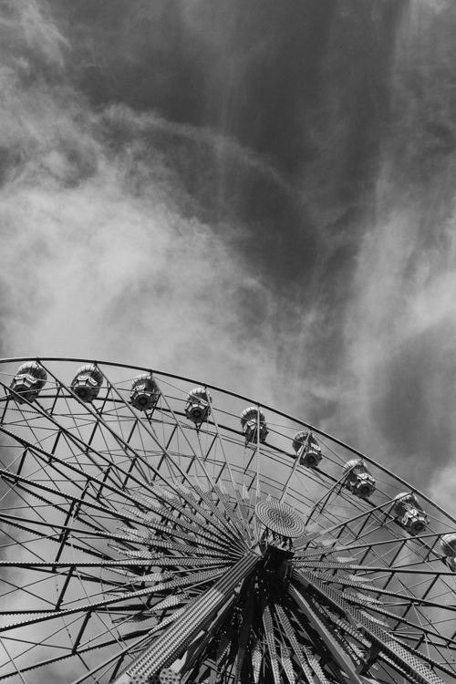 Free Black and white shot of a ferris wheel with a dramatic cloudy sky backdrop. Stock Photo