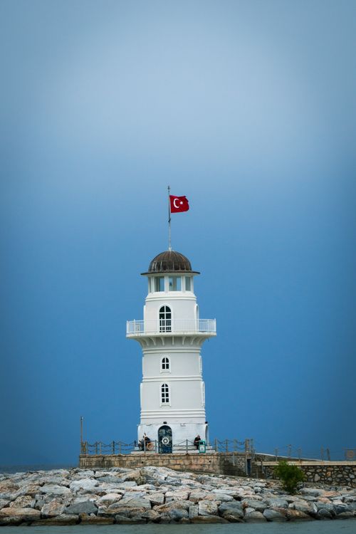 Free Dramatic view of a white lighthouse under a blue sky with a Turkish flag on top. Stock Photo
