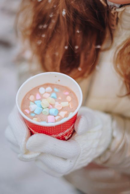 Warm winter scene with a woman holding hot chocolate topped with colorful marshmallows.