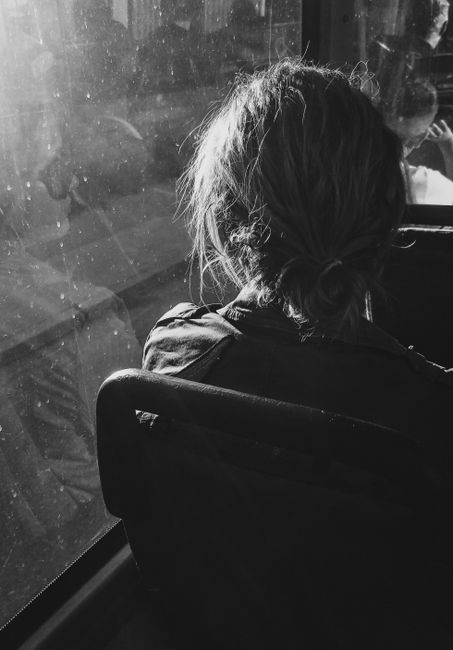 Black and white photograph of a person sitting on a bus, gazing out the window in thoughtful silence.