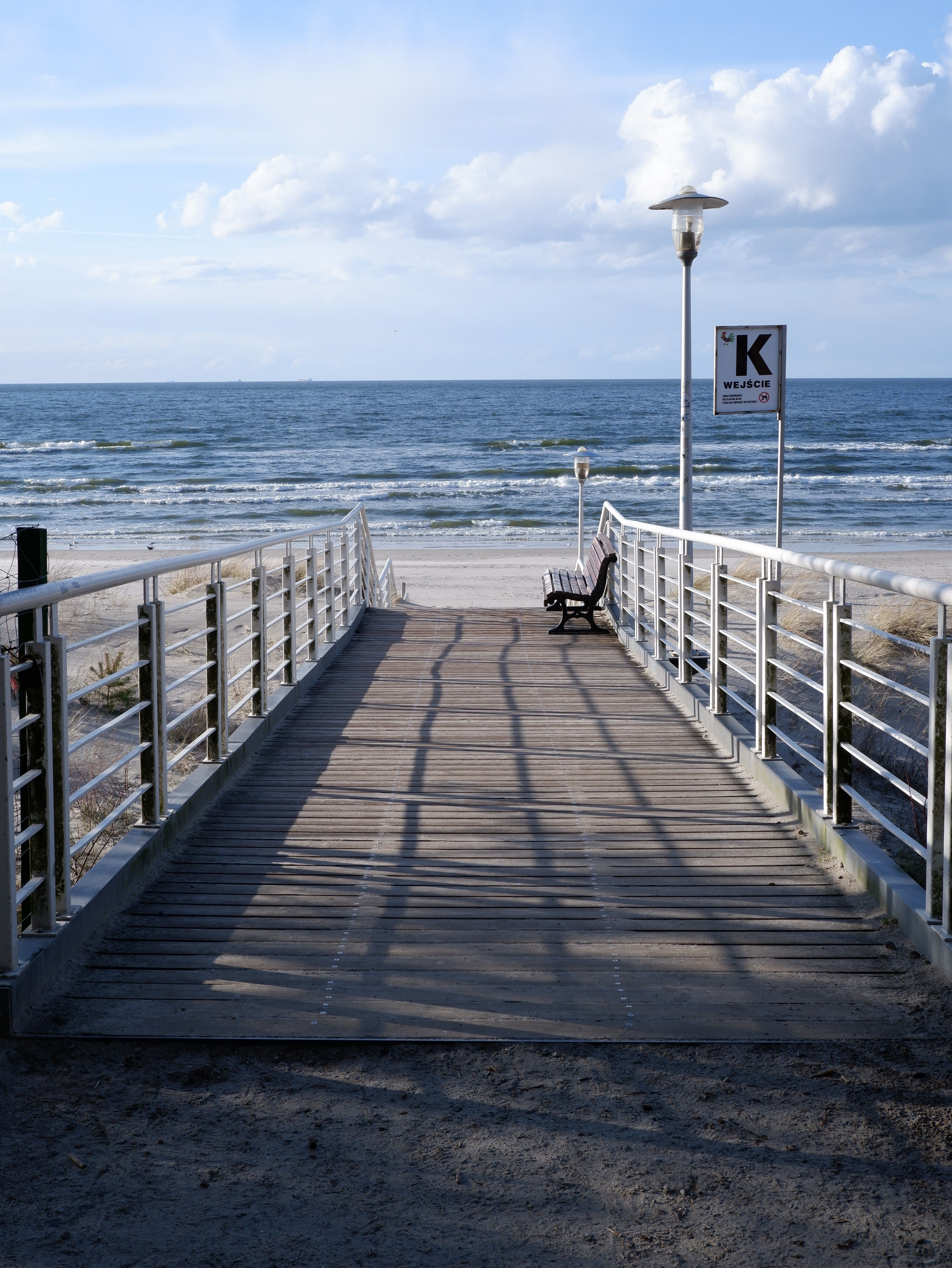 Peaceful coastal wooden walkway leading to Misdroy beach with blue sea and sky.