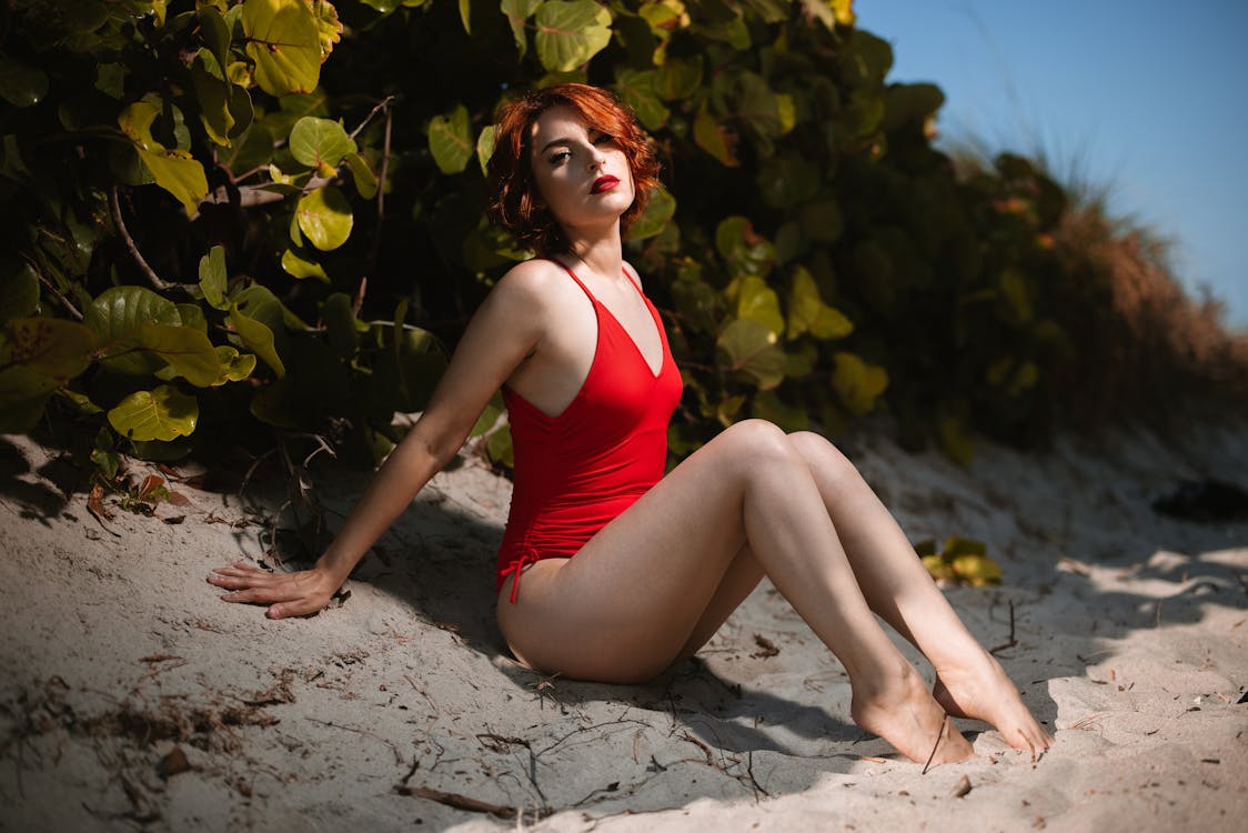 Free A Woman in Red Swimsuit Sitting on the Beach Sand Stock Photo