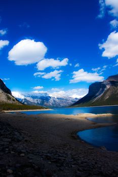 Stunning view of Lake Minnewanka with snowcapped mountains and blue sky in Banff National Park, Canada.