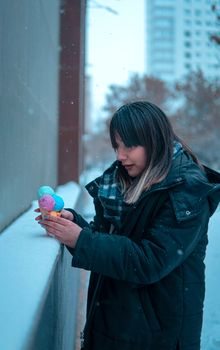 Woman in warm clothing holding colorful ice cream cone on a snowy day in the city.