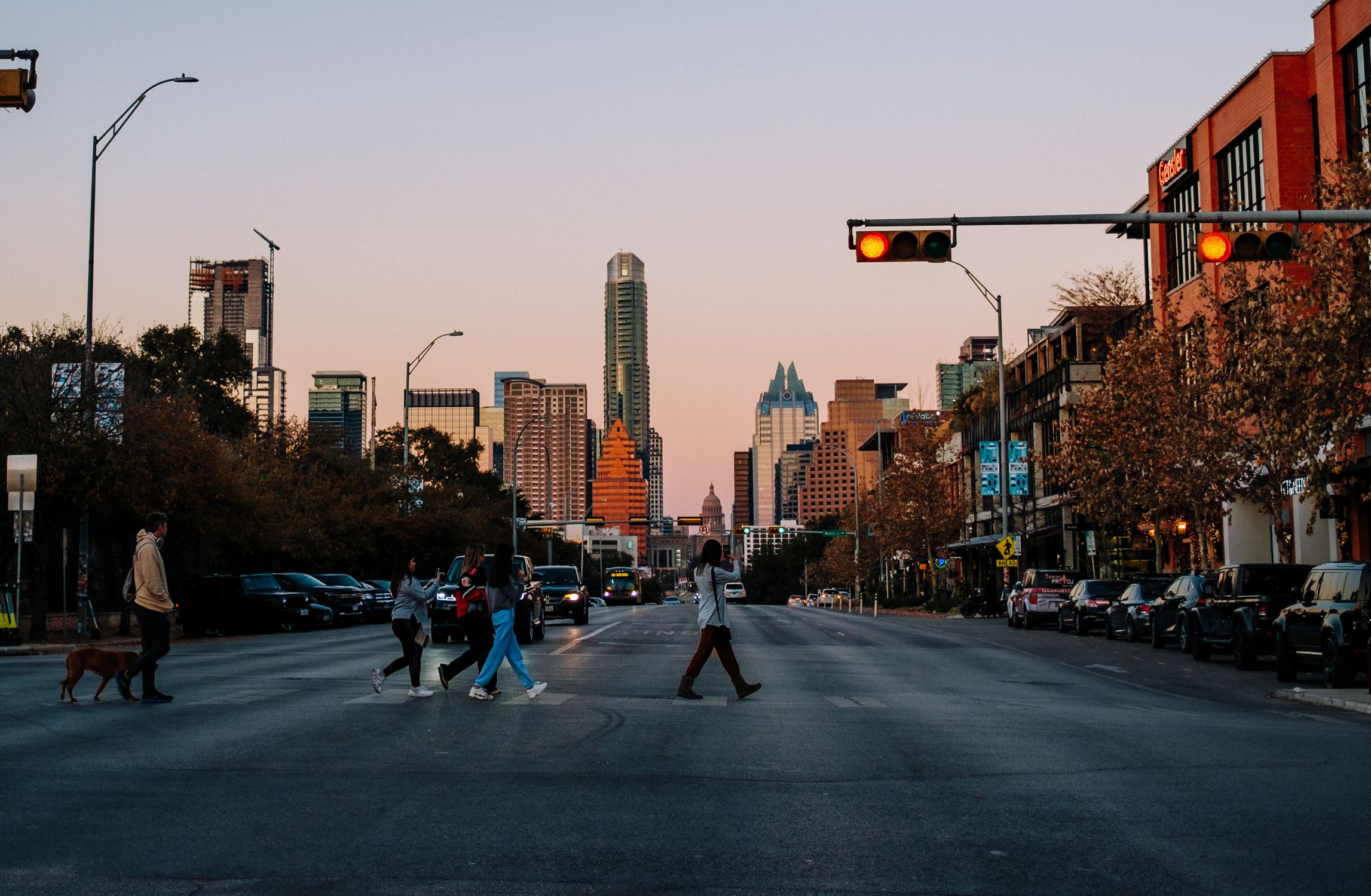 People crossing a city street in Austin, Texas at sunset with the skyline in the background.