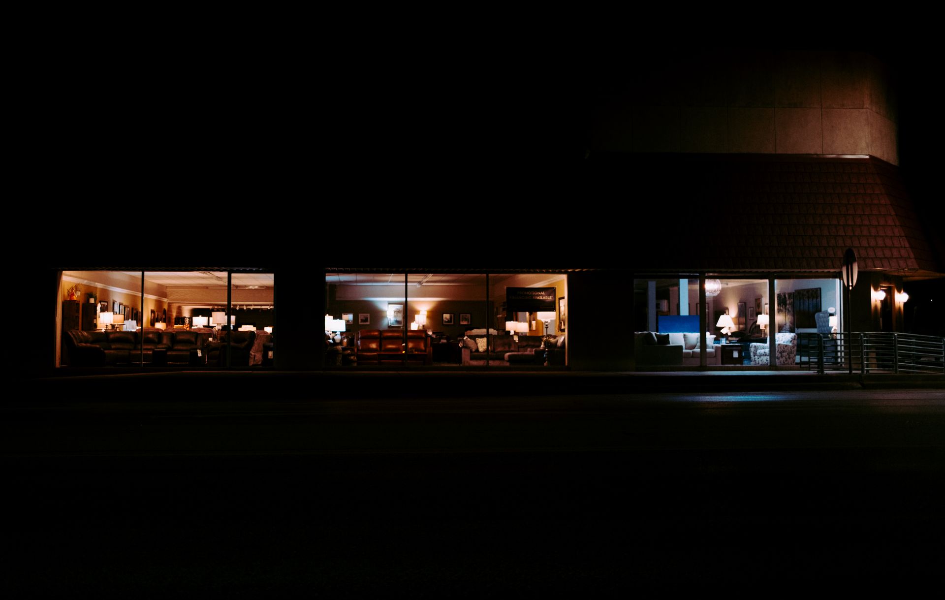 A cozy view of an illuminated furniture store showcasing sofas and displays at night.