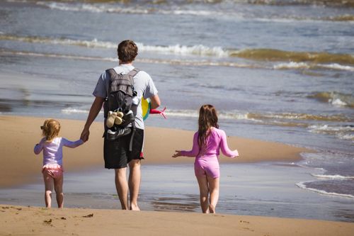 Free Father and two daughters walking along a sandy beach, enjoying a summer day by the sea. Stock Photo