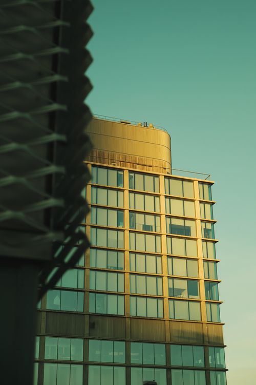 Free A modern skyscraper with glass and steel facade captured in golden sunset light, featuring geometric shapes. Stock Photo