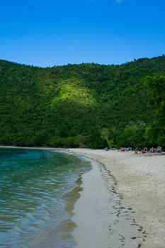 A serene beach scene featuring a curving shoreline against lush green hills under a clear blue sky.