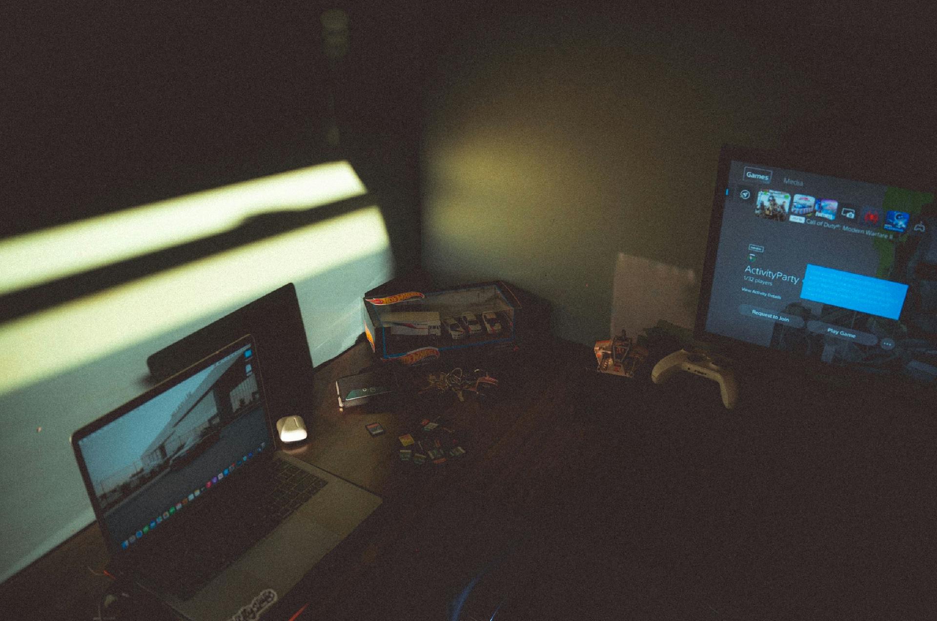 Dark room with a laptop and gaming console creating a moody tech atmosphere.