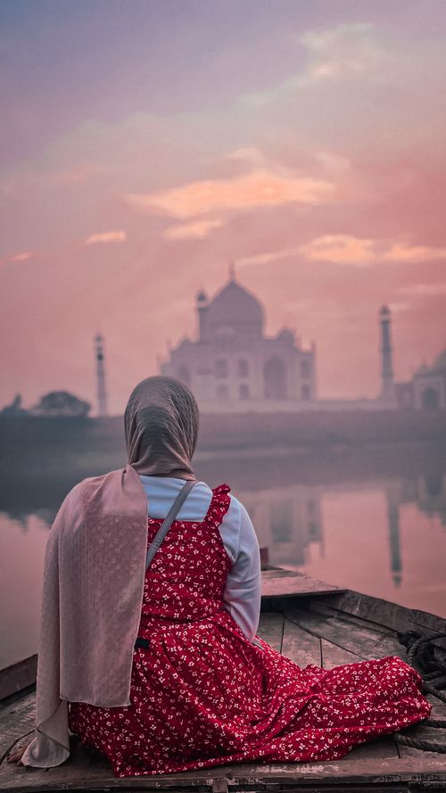 Free A serene moment with a woman in a red dress admiring the Taj Mahal at sunset, capturing a tranquil and reflective scene. Stock Photo