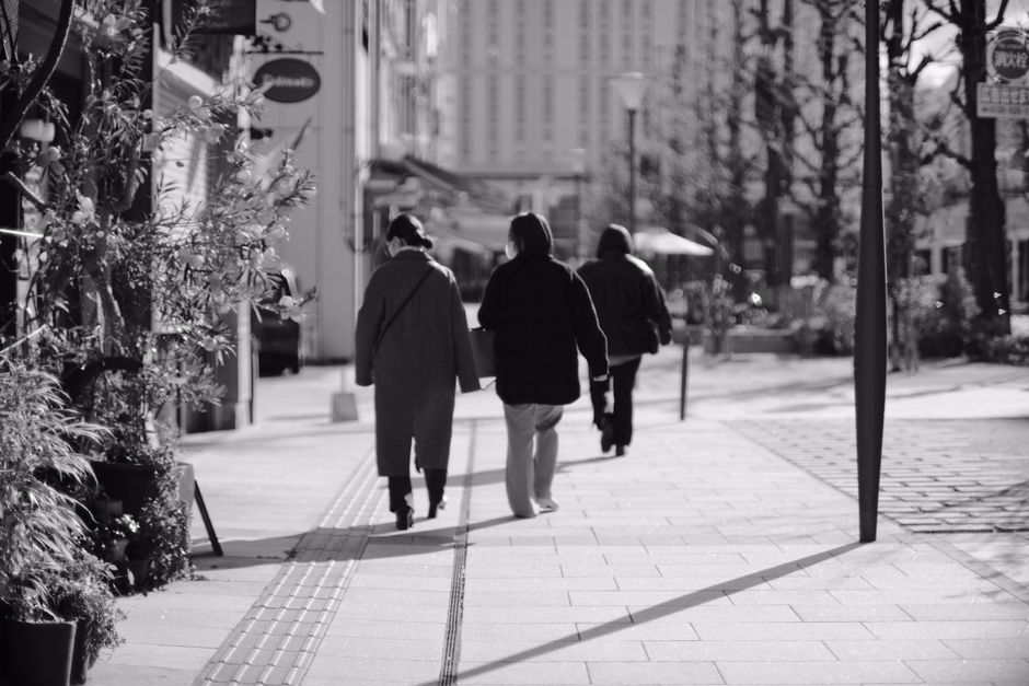 白黒の街の通りを歩く歩行者の後ろからのビュー。