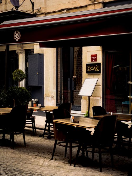 Free Elegant outdoor café setting with tables, chairs, and cobblestone street. Stock Photo