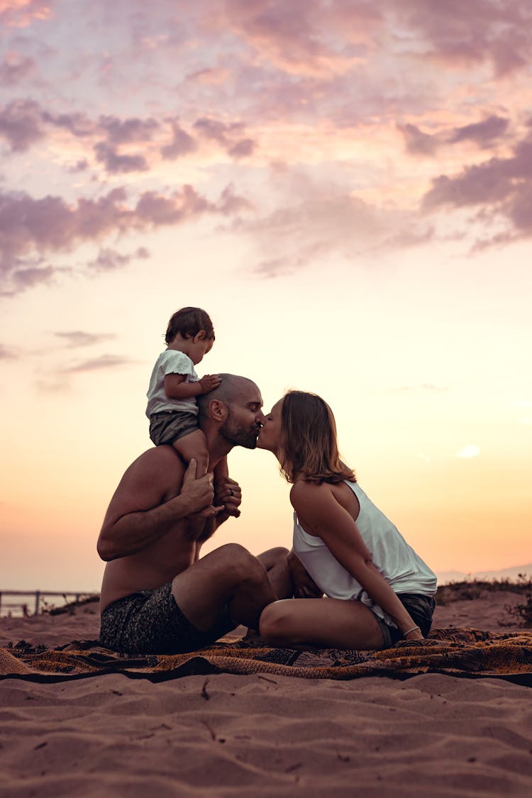 Man Kissing Woman At Sunset With Toddler On His Shoulders