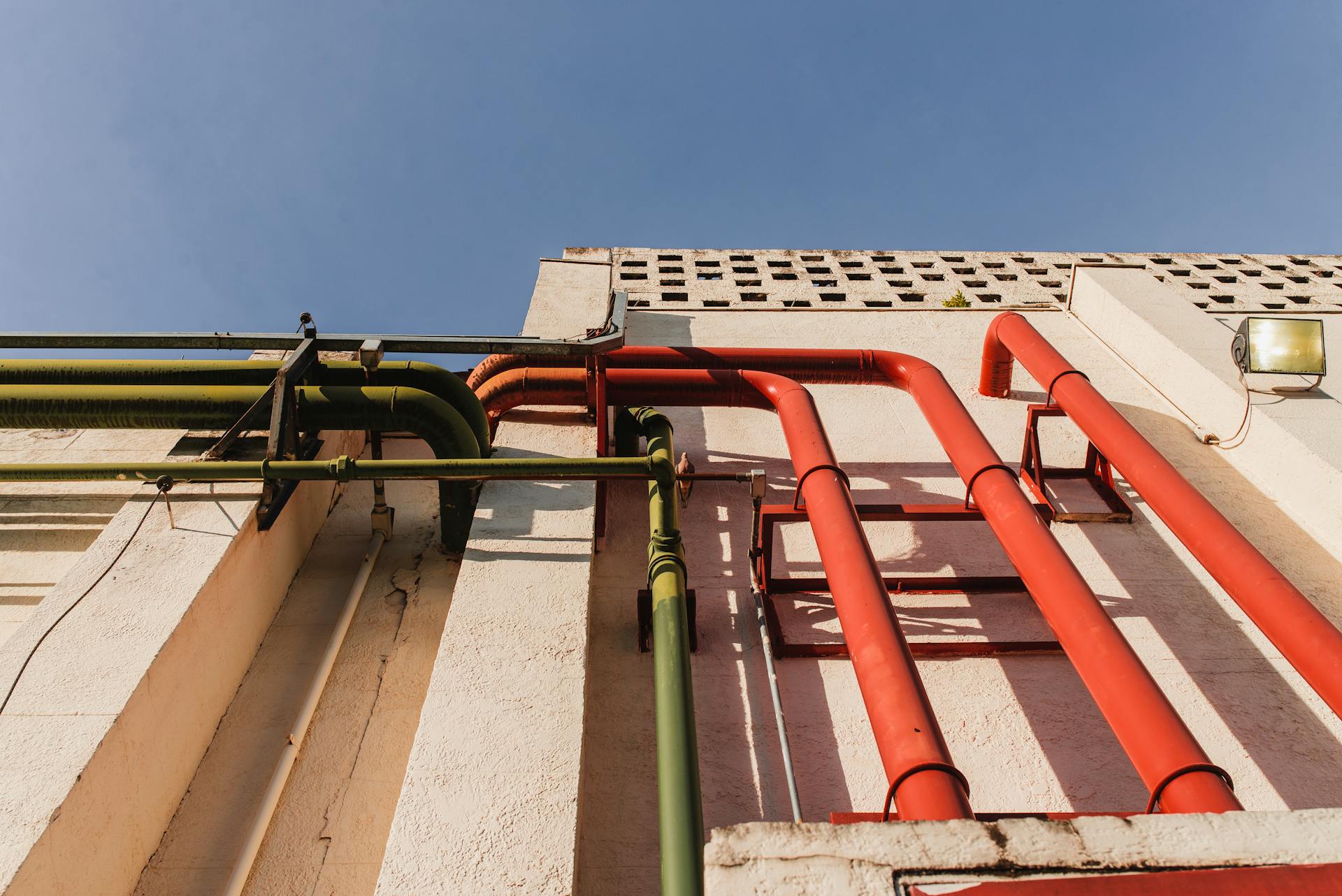 Close-up of vibrant red and green pipes on a sunlit urban building wall.