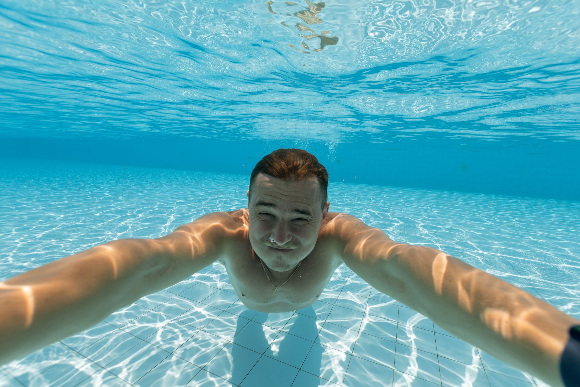 Man smiling underwater in a bright pool showing aquatic serenity.