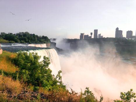 Breathtaking sunrise view of Niagara Falls with mist and city skyline.